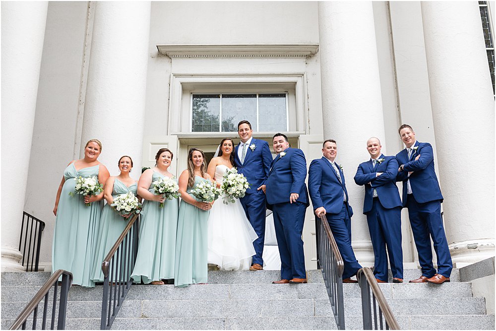 wedding party poses for portrait at the top of the steps, in front of columns at St. Peter's Catholic Church in Richmond, va immediately following classic southern wedding ceremony