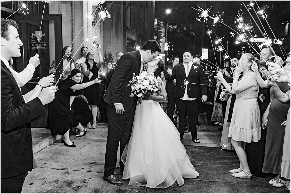 bride and groom kiss during grand exit while guests wave long sparklers above their heads at classic southern wedding in Richmond, va