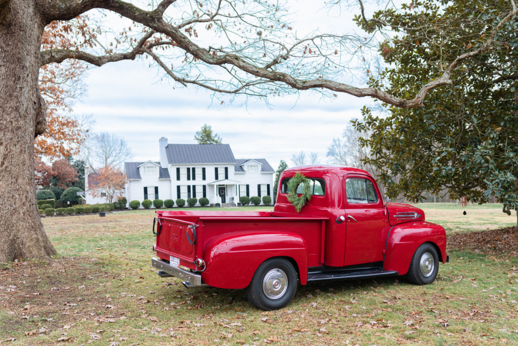 Classic red ford truck parked on sweeping green lawn in front of Whitewood, a historic estate wedding venue in the heart of Virginia.