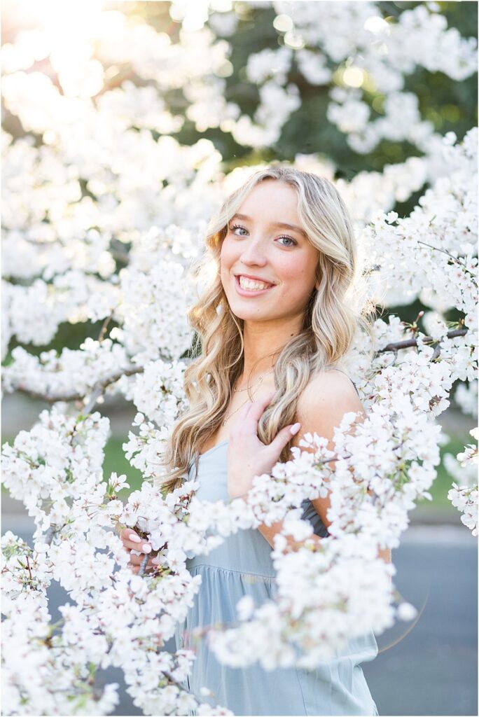Ellen stands surrounded by pastel cherry blossoms during her spring senior portrait session