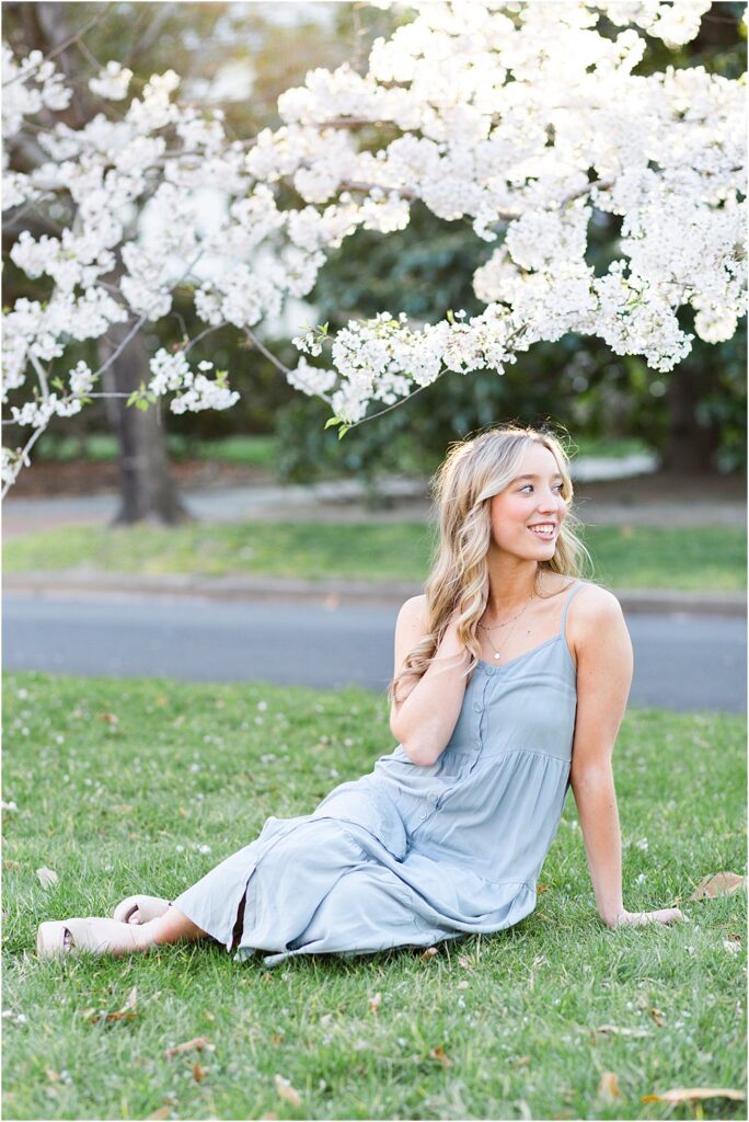 Ellen sits on the grass beneath cherry blossoms during her spring senior portrait session