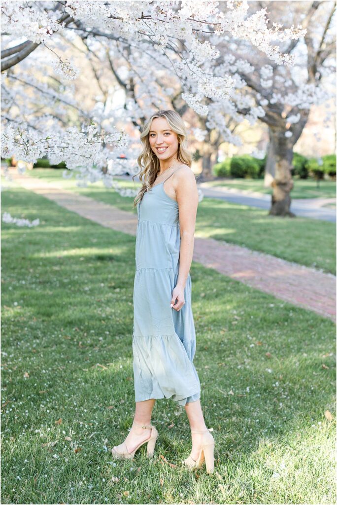 Ellen stands beneath cherry blossoms during spring senior portrait session