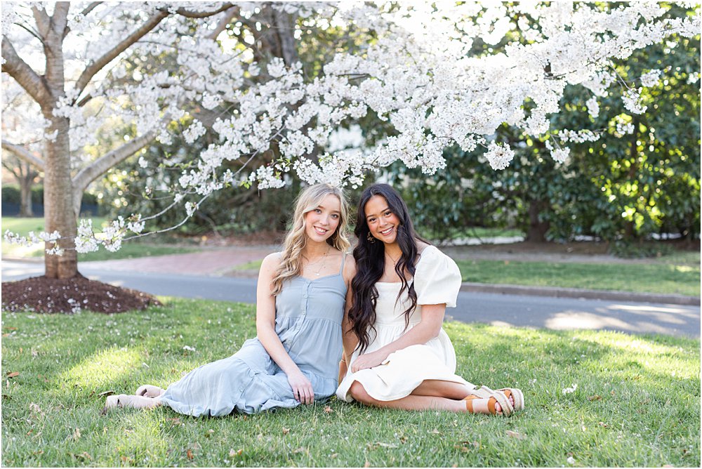 Kiera and Ellen, dressed in pastel dresses, sit on the grass beneath the cherry blossoms in RVA