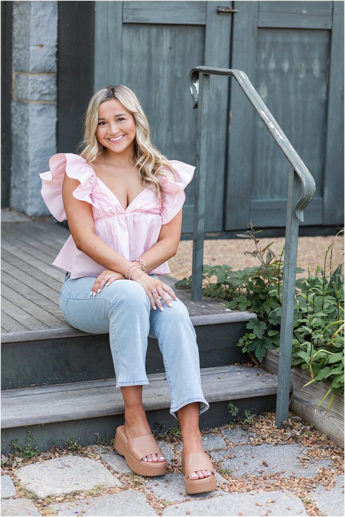 High school senior, wearing pale blue denim jeans and blush puffed butterfly sleeve blouse, poses for a photo in Maymont Park during bright and bubbly senior portrait session in Richmond, VA
