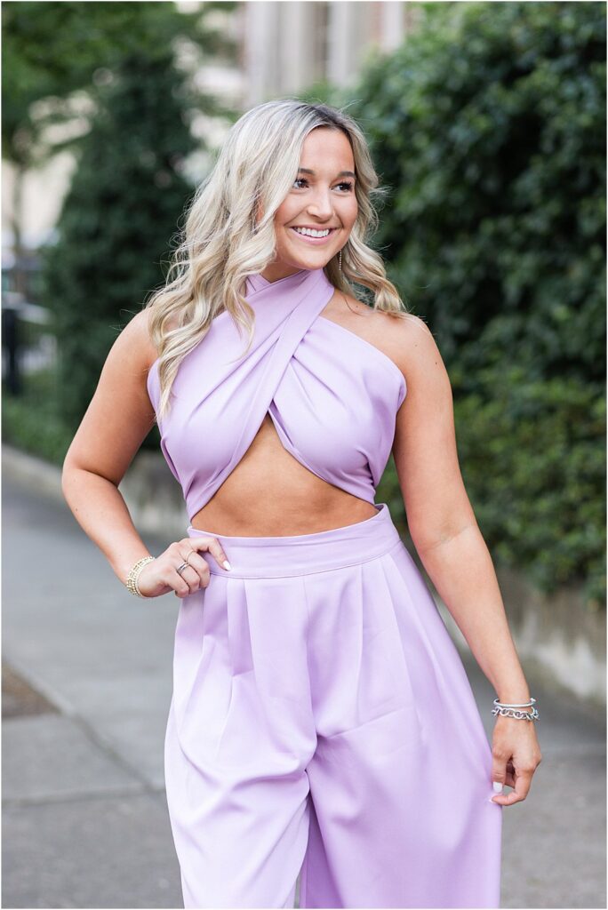 High school senior, dressed in lilac jumpsuit, poses for a photo on Monument Avenue during bright and bubbly senior portrait session in Richmond, VA