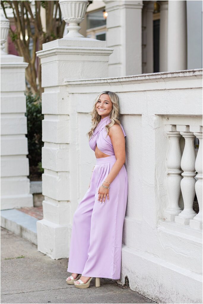 High school senior, dressed in lilac jumpsuit, poses for a photo on Monument Avenue during bright and bubbly senior portrait session in Richmond, VA