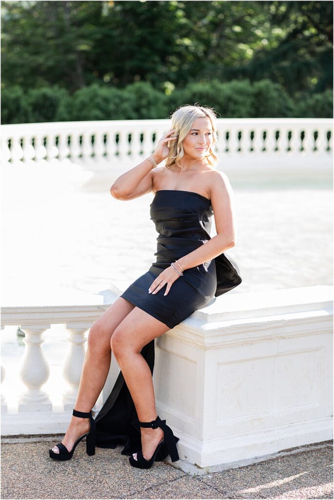 High school senior poses for a photo in black mini dress and heels in front of fountain during bright and bubbly senior portrait session in Richmond, VA
