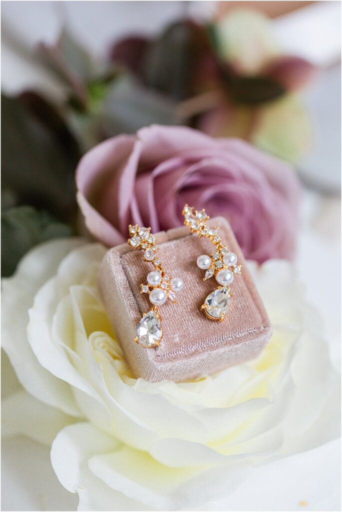 Detail shot - gold, pearl and crystal earrings in blush velvet box, resting on top of a white rose.