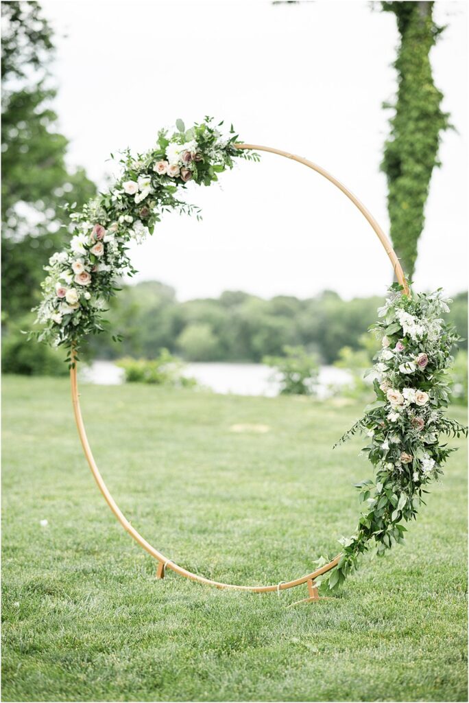 Circle arch adorned with assymetrical greenery and blooms, served as the alter on Upper Shirley's Lawn overlooking the James River during a modern romantic wedding reception in Charles City, VA