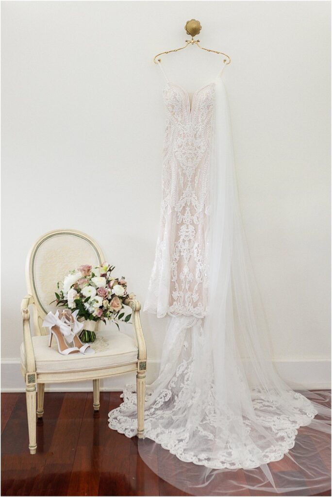 Stephanie's wedding dress and veil, hanging on a gold hanger next to a chair holding the bridal bouquet and wedding accessories.