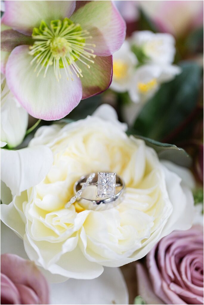 Emerald cut engagement ring and two white gold wedding bands rest atop lush creamy white and mauve blooms.