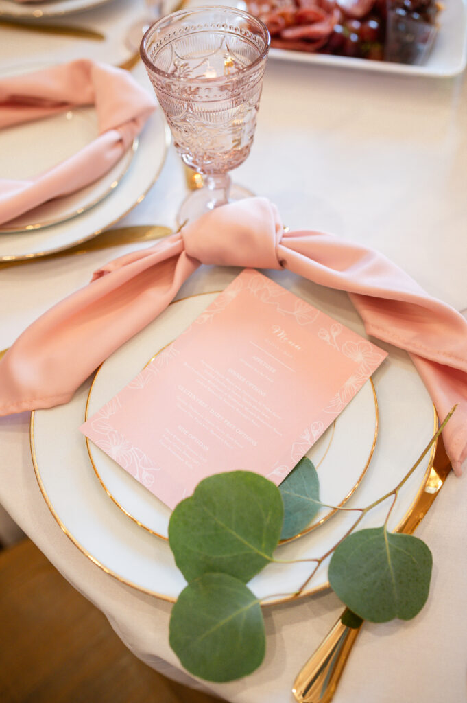 Reception Place seating - blush menu on white dinnerware rimmed with gold, gold flatware and blush glassware. Blush menu with white writing.
