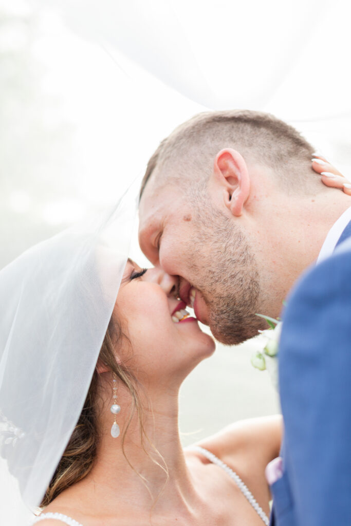 bride and groom kiss beneath flowing wedding veil romantic barn wedding day