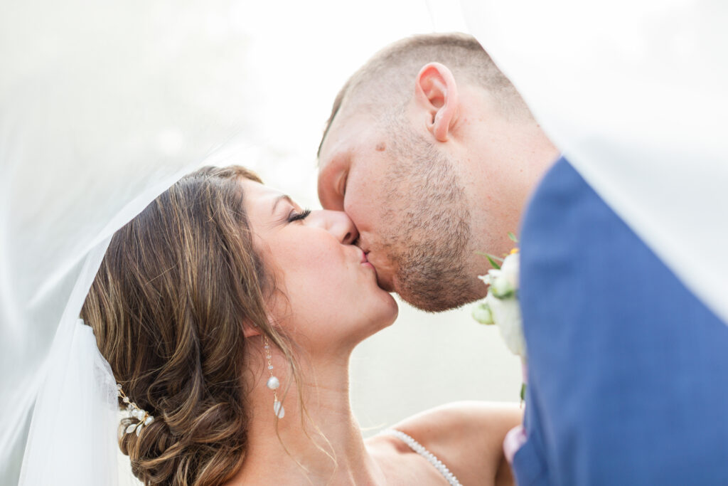 bride and groom kiss beneath flowing wedding veil romantic barn wedding day