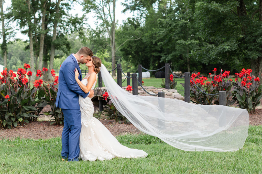bride and groom kiss in Altria Farm gardens, brides veil floats I the wind during during romantic barn wedding day