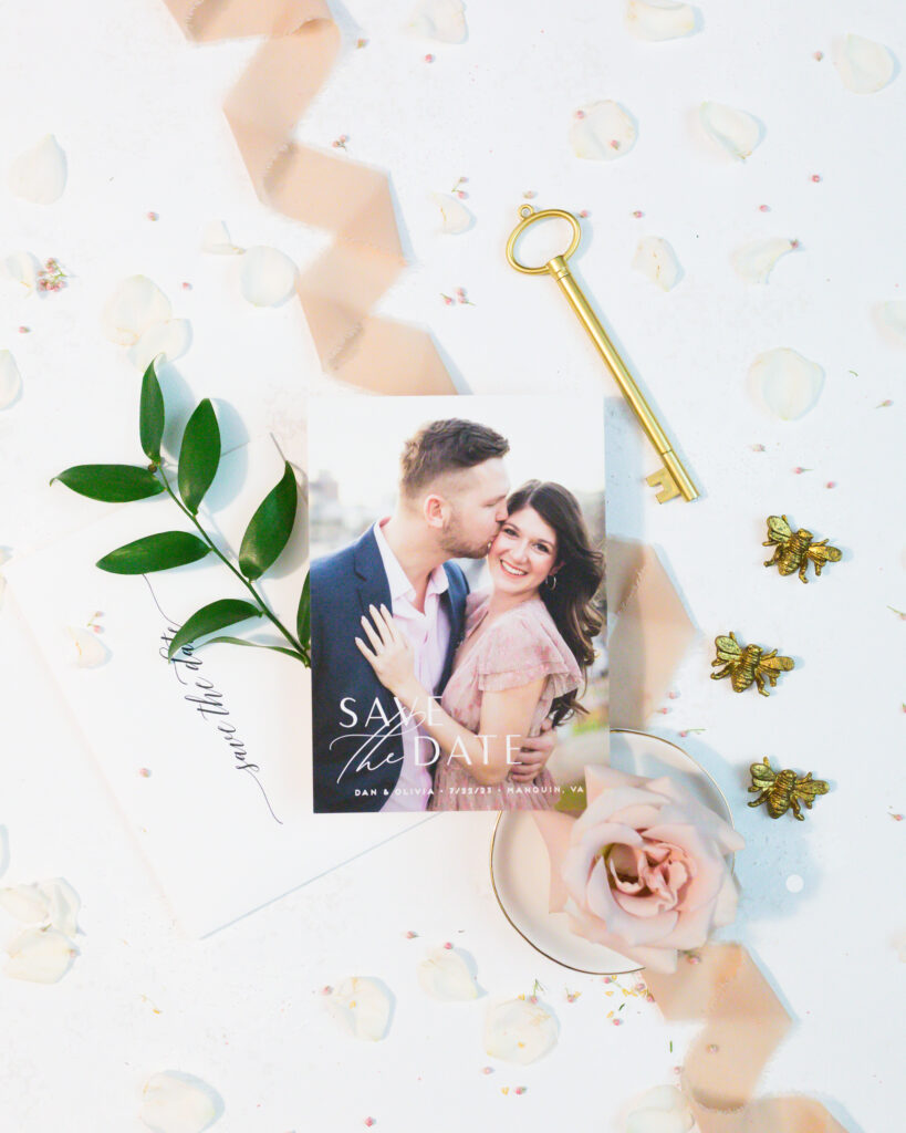 flat lay: wedding invitation details:blush ribbon, gold wax seals, white paper with blush writing, blush blooms and greenery
