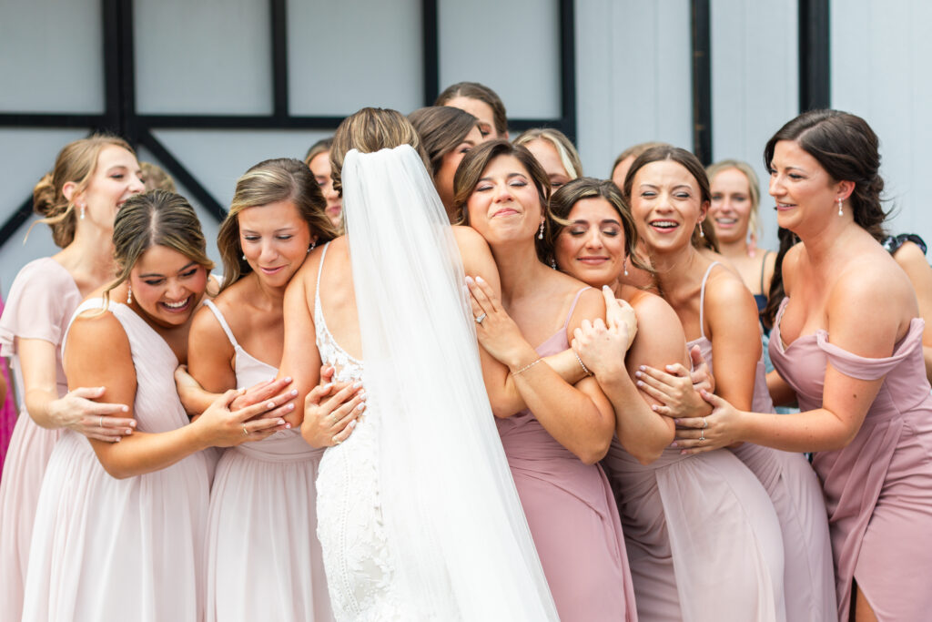 the bridesmaids embrace the bride during wedding party first look on romantic barn wedding day in King William, VA