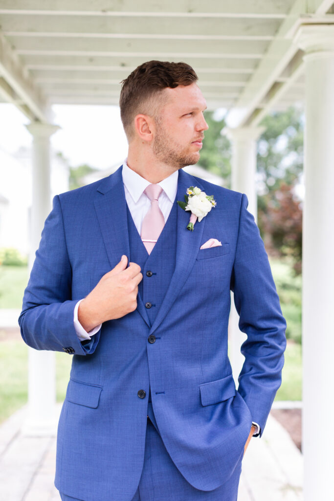 Groom portrait - he touches his lapel and glances to the side during romantic barn wedding day in King William, VA