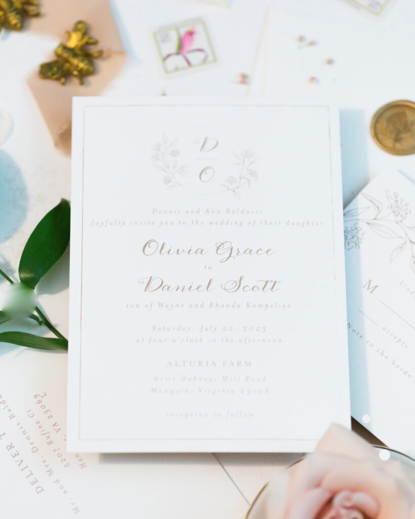 flat lay: wedding invitation details:blush ribbon, gold wax seals, white paper with blush writing, blush blooms and greenery