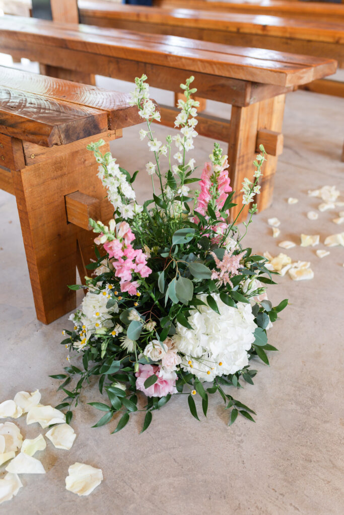 large ground sprouts consisting of greenery, white blooms, and blush blooms, lined wood pews to form an aisle during romantic barn wedding in King William, VA