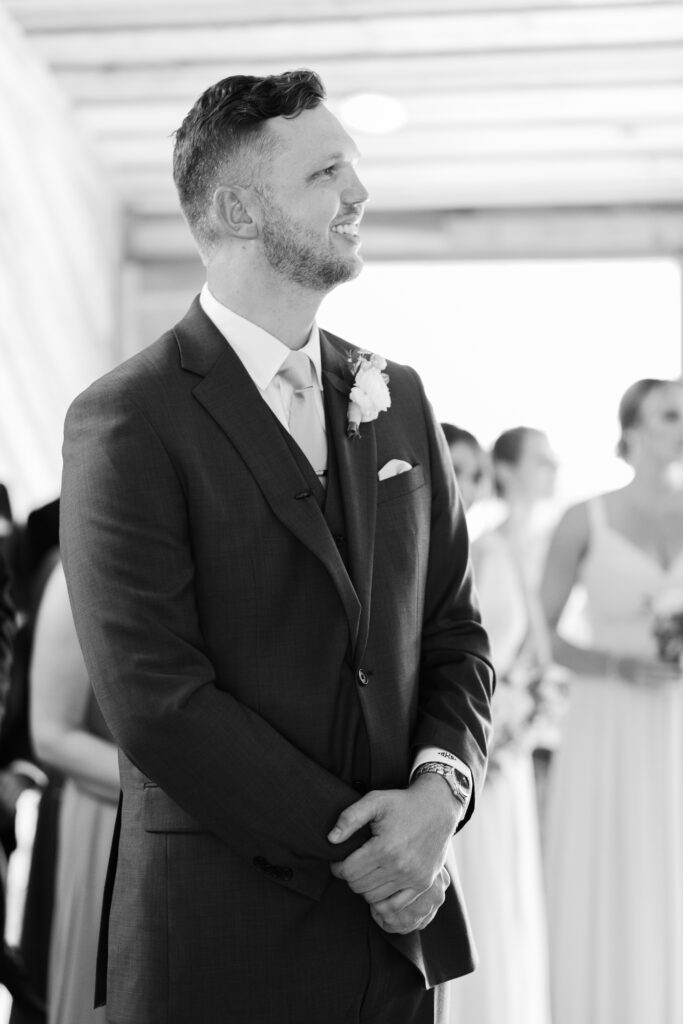 The groom smiles as he sees his bride for the first time as she was down the aisle during romantic barn wedding in King William, VA