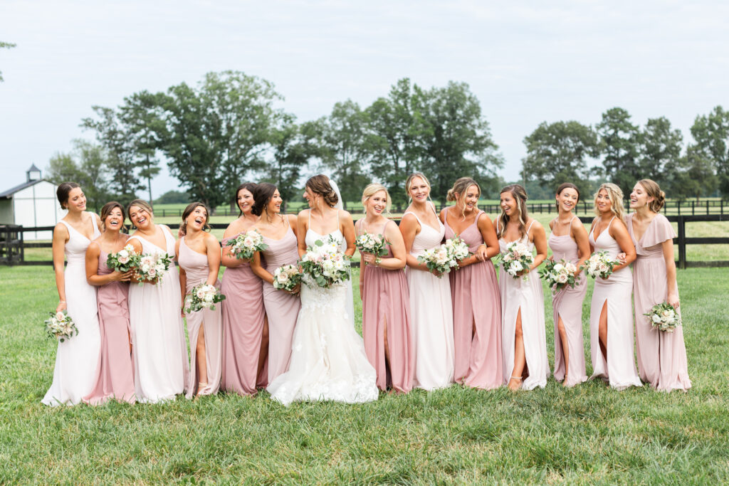 bride and bridesmaids smile and laugh while hooding bouquets during romantic barn wedding.