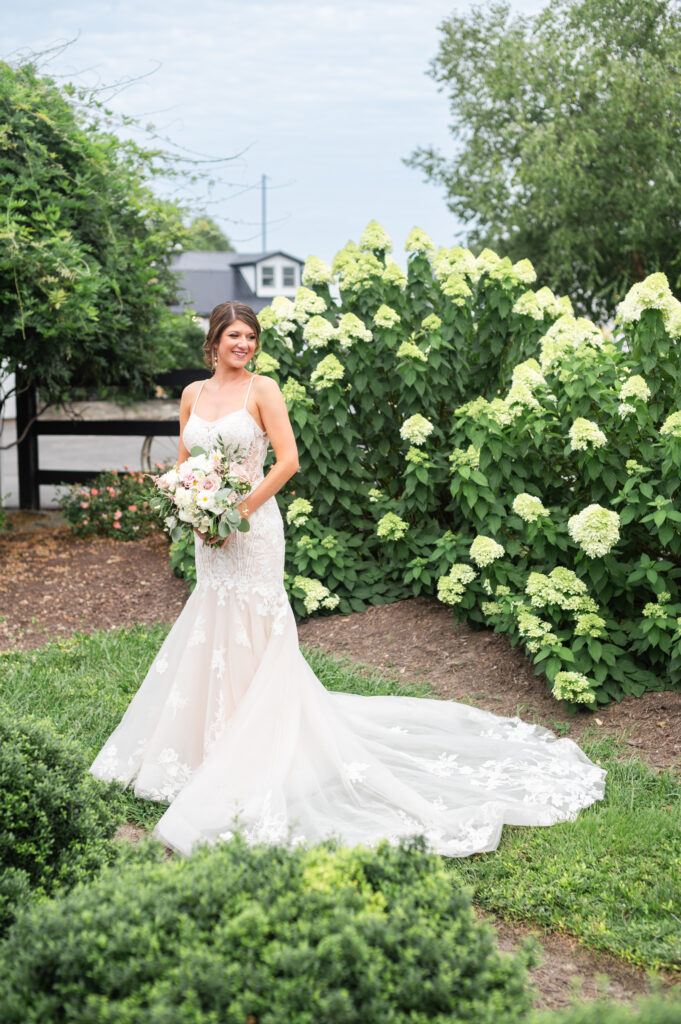 Bride holds bouquet and showcases her stunning romantic wedding dress in the gardens at Altria Farm romantic barn wedding