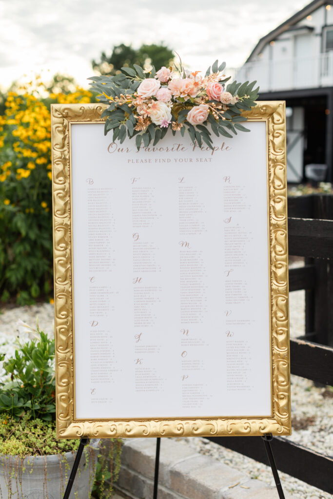 Seating chart in gold frame with blooms on top during romantic barn wedding