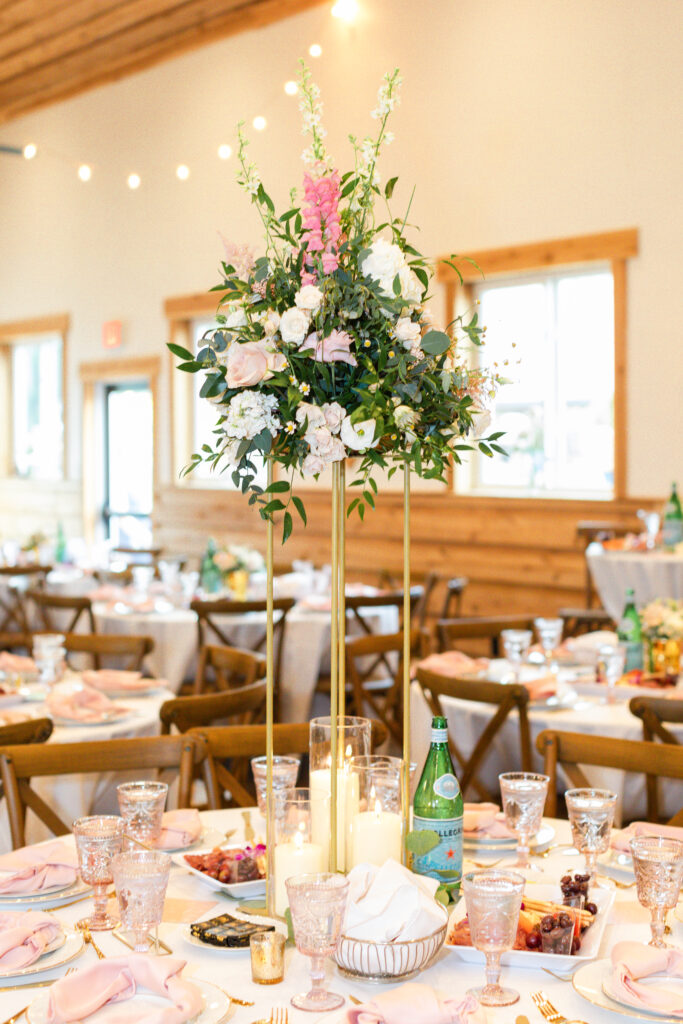 Tall gold stands with blush and white flowers, and greenery adorned romantic barn wedding reception tables.