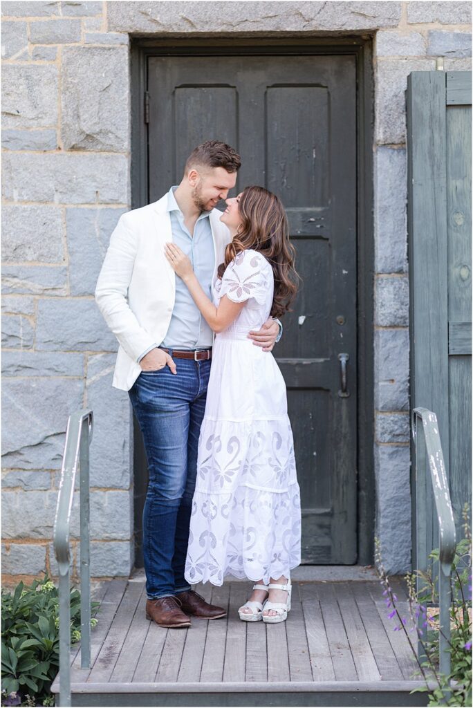 The couple, smiling and nose to nose, prepare to kiss beneath in front of a stone building during their effortlessly chic engagement session.