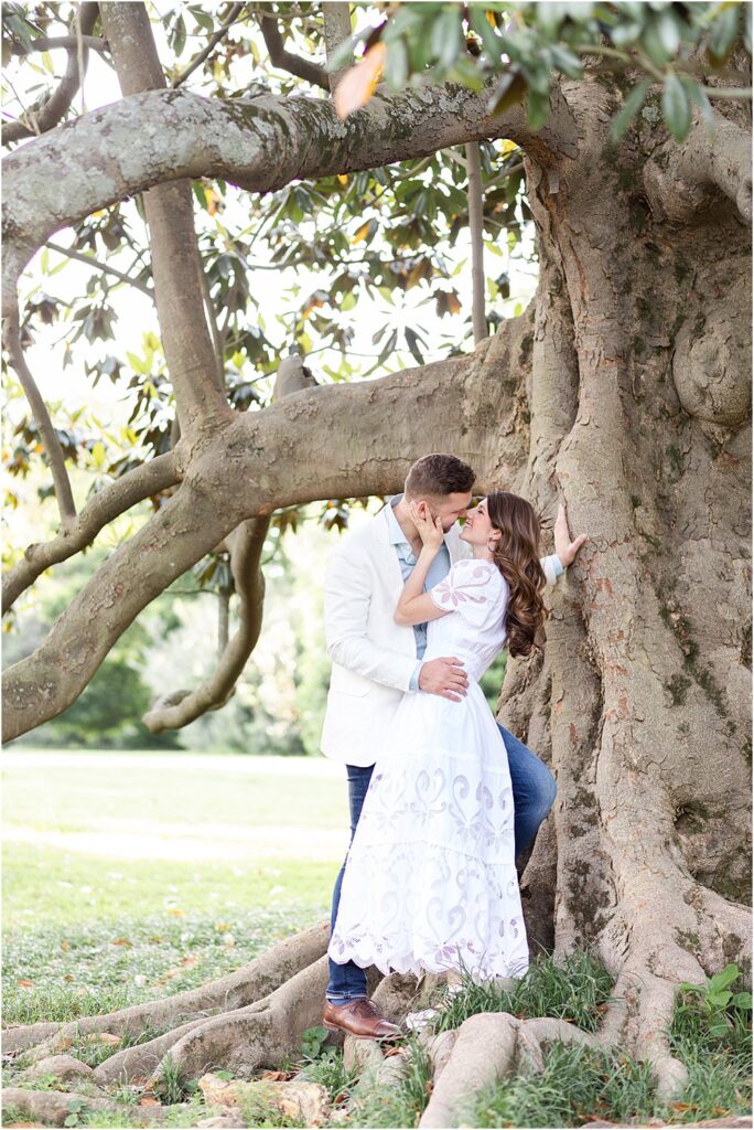Olivia gently caressing dan's cheek as the couple stands nose to nose, preparing to kiss, beneath an ancient and gnarled tree at Maymont Park.