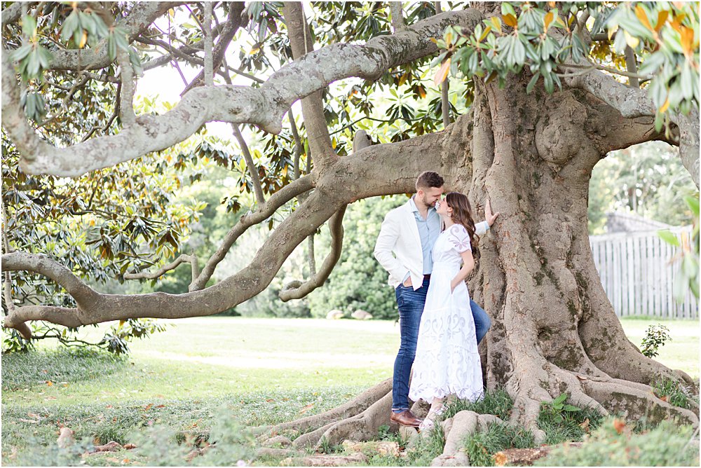 The couple casually leans against the trunk of an ancient and gnarled tree as they gaze longingly at one another.