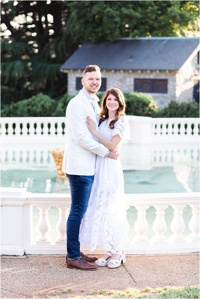 The couple cuddles, Olivia's hand on Dan's chest, as they pose and smile for the camera during their effortlessly chic engagement session at one of Maymont Park's fountains