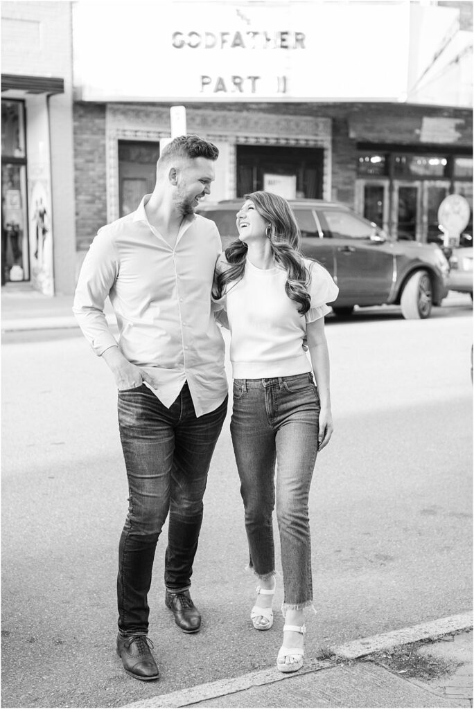 The couple looks at each other and laughs as they cross Cary Street during their effortlessly chic engagement session in RVA
