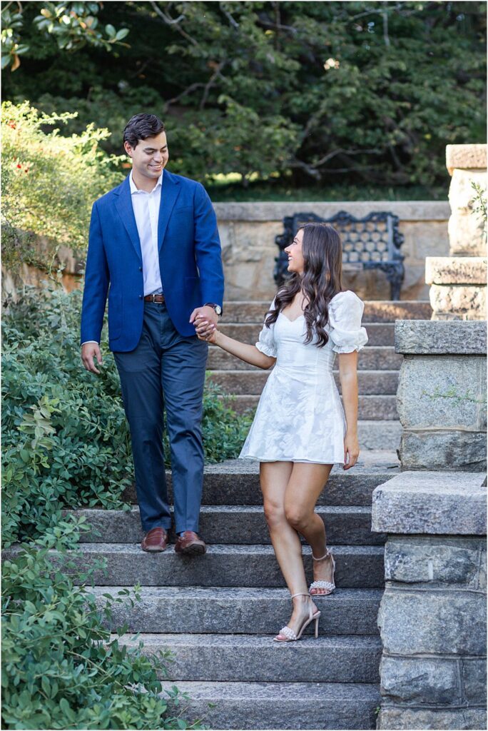 Gabriella and Raphael hold hands, smiling, as they descend stairs during classic engagement session at Maymont Park in Richmond, VA.