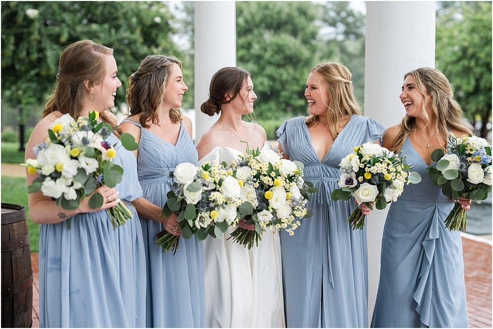 bridesmaids and bride standing outside the Estate at Independence  wearing light blue gowns and holding white roses floral bouquet