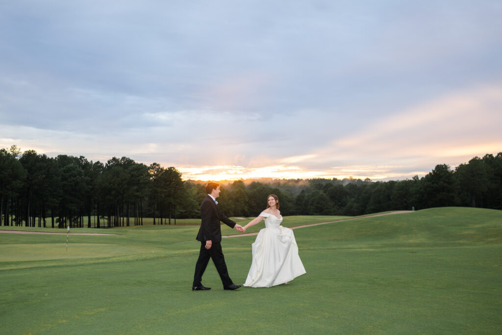 A bride and groom walk hand in hand at sunset on the golf course at the Estate at Independence