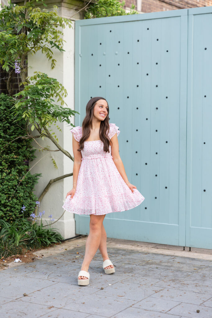 girl wearing pink dress next to blue gate during senior portraits