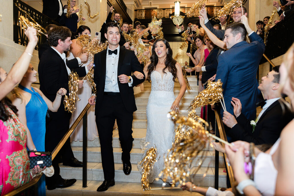 bride and groom exit their reception while their guests wave pom pom streamers to send them off